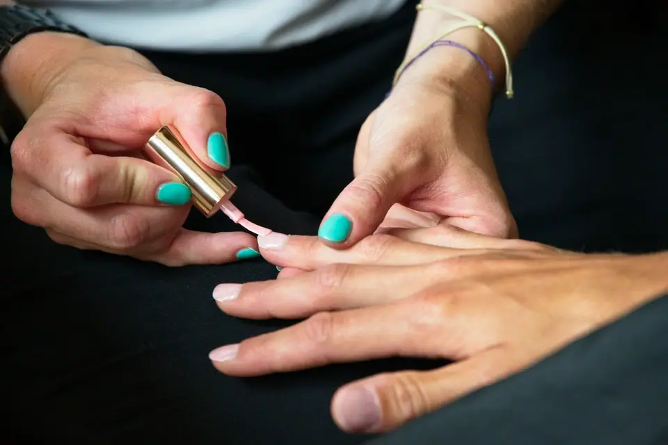 Manicurista pintando las uñas de una clienta con esmalte claro.