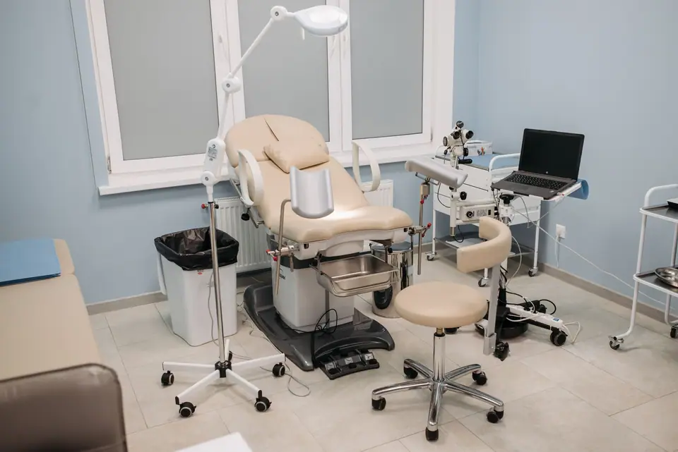 Consultorio de ginecología con camilla de examen, banqueta y equipamiento médico.