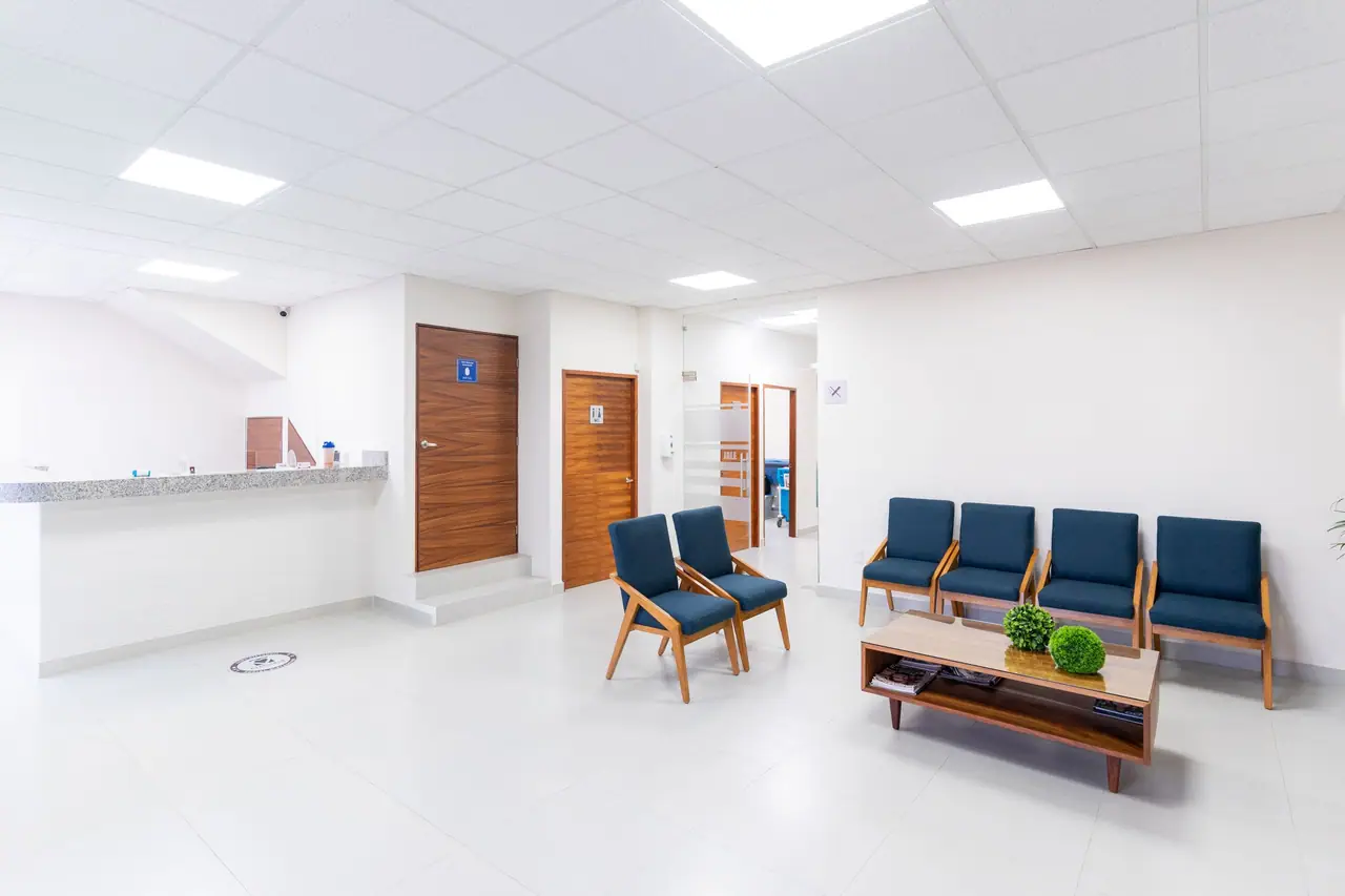 Recepción luminosa de una clínica moderna con sillas azules en la sala de espera, sin personas.