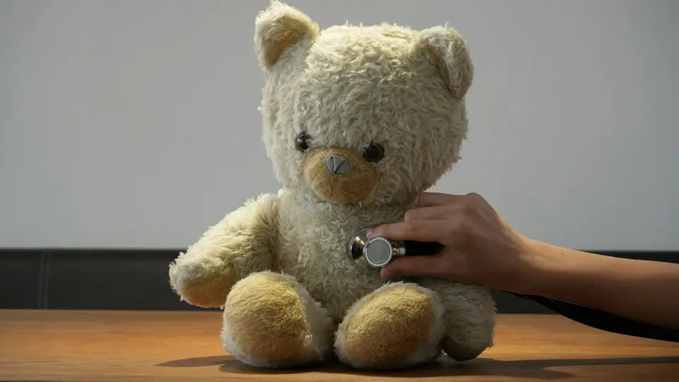 Mano sosteniendo un estetoscopio sobre el pecho de un osito de peluche.