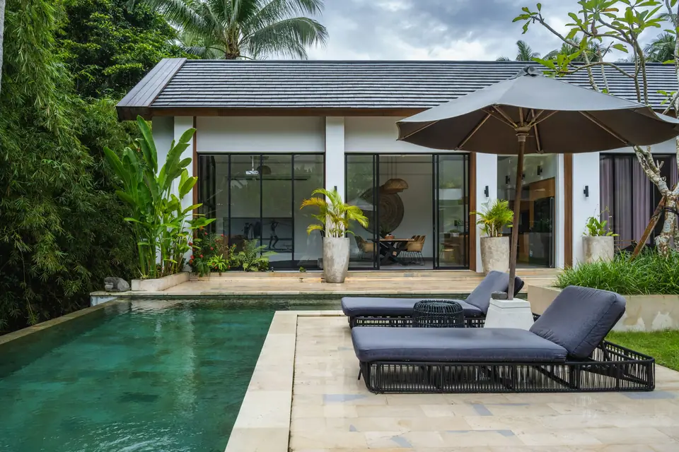 Casa con piscina, reposeras y jardín tropical.