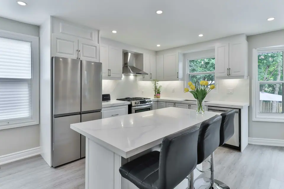 Cocina blanca con isla de mármol, banquetas y heladera de acero.