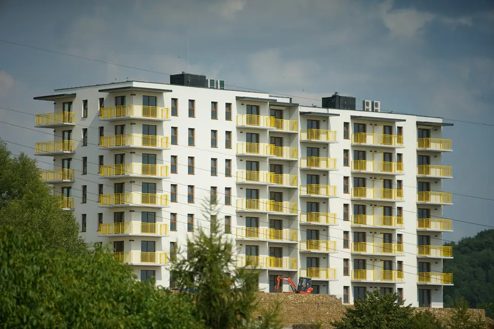 Edificio de departamentos moderno blanco con balcones amarillos rodeado de verde.