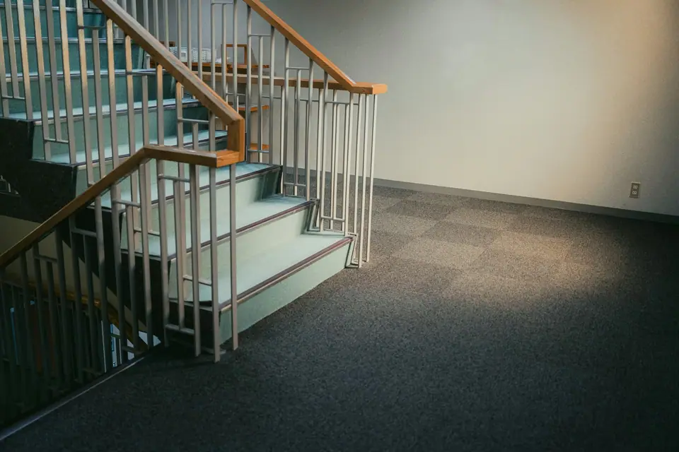 Escalera interior con baranda de madera y metal sobre un piso alfombrado.