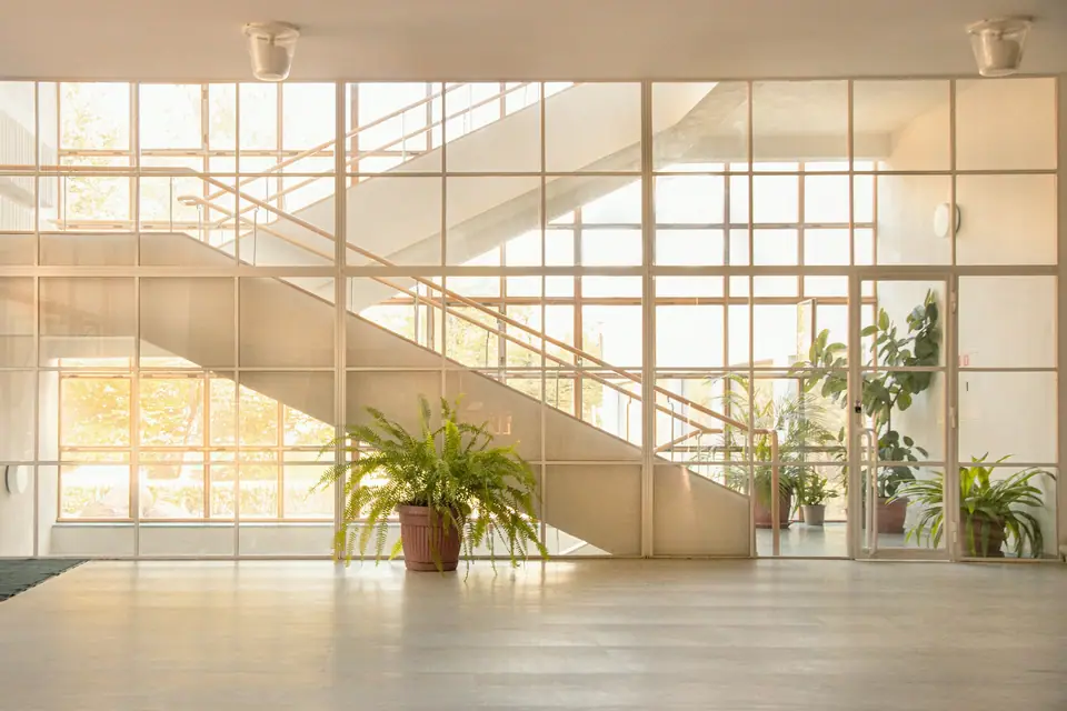 Oficina vacía y luminosa con ventanales, escalera de vidrio y plantas.