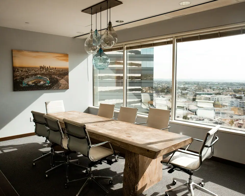 Sala de reuniones vacía con mesa de madera, sillas ejecutivas y vista a la ciudad.