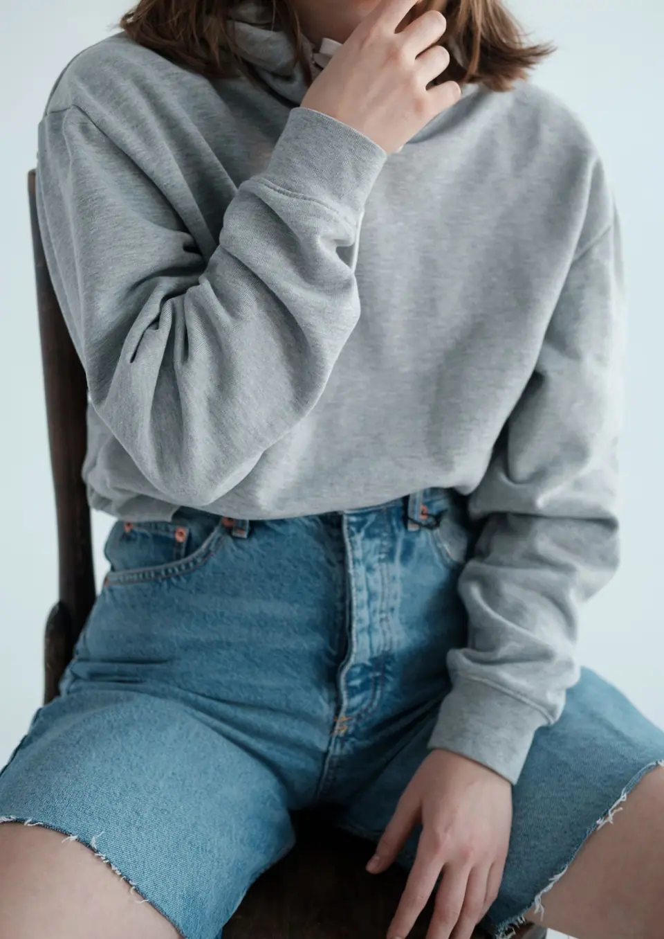 Persona sentada con buzo gris con capucha y short de jean sobre fondo claro