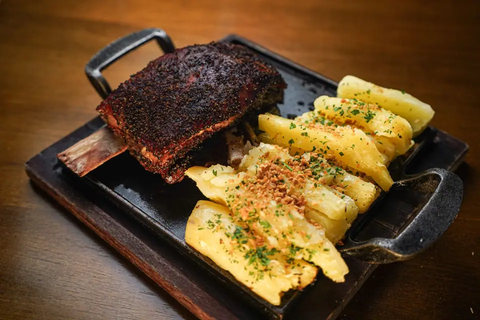 Tira de asado servida en plancha de hierro con mandioca hervida
