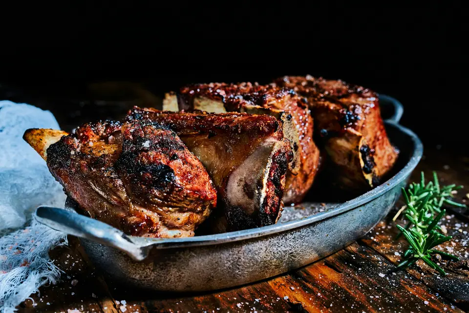 Costillas de res asadas al horno en una fuente metálica con romero y sal gruesa