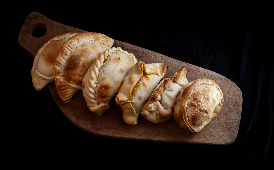 Seis empanadas horneadas sobre una tabla de madera, con fondo oscuro