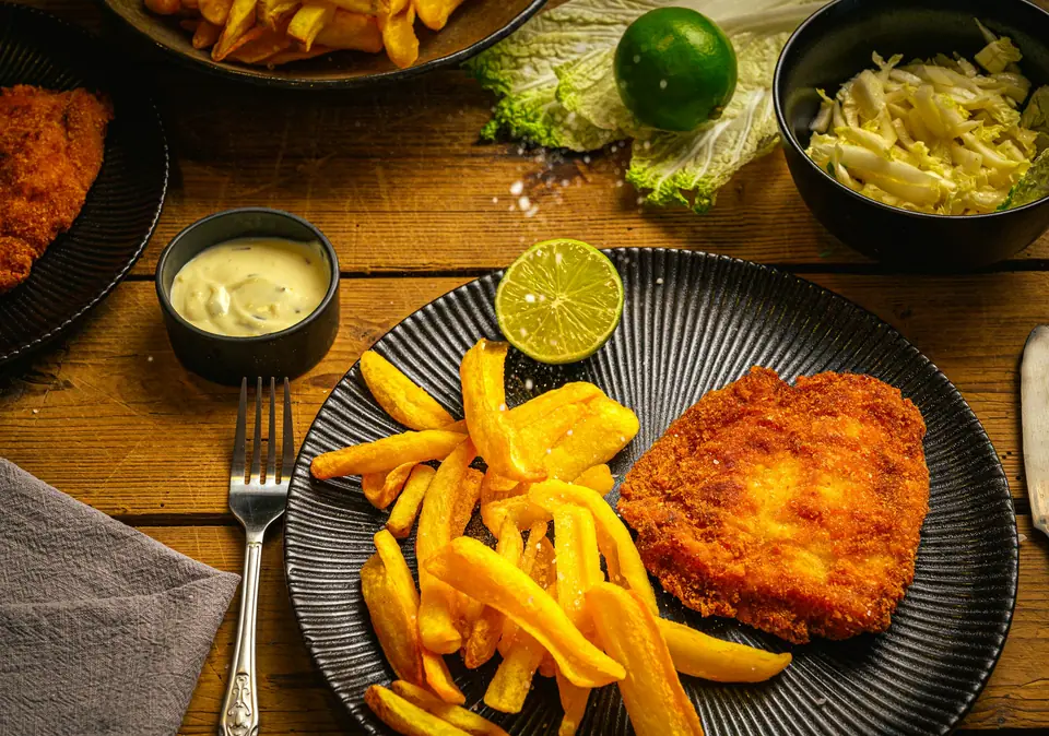 Milanesa con papas fritas, limón y ensalada sobre una mesa de madera