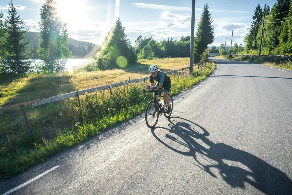 Ciclista de espaldas pedaleando por una ruta rodeada de verde.