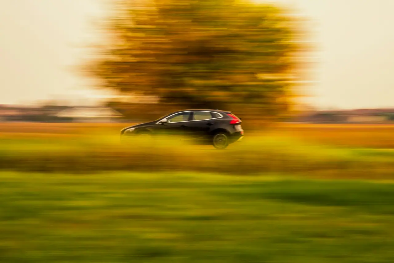 Auto oscuro circulando por una ruta entre campos al atardecer, con efecto de movimiento.