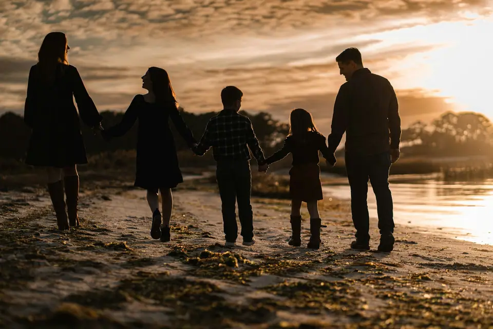 Familia de espaldas caminando de la mano por la playa al atardecer.